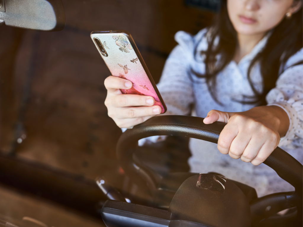 Woman holding her steering wheel in one hand and her phone in the other.